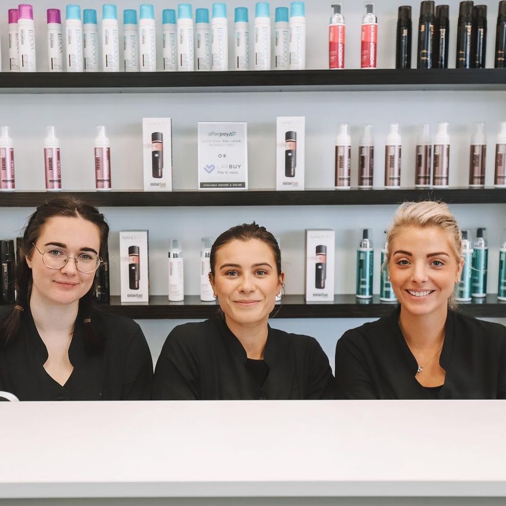 Spray tan technicians with MineTan products in the background